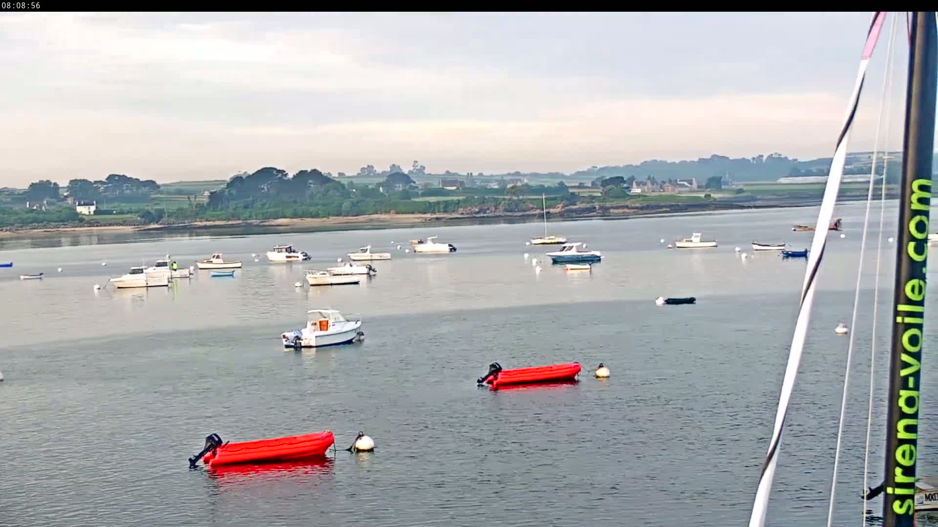 Many small motorboats are moored in a calm body of water under a mostly cloudy sky, with a distant shoreline visible in the background.
