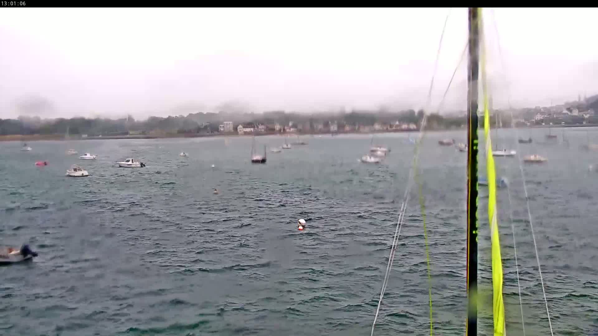 Numerous small boats are scattered across a choppy body of water on a foggy day, with a distant shoreline visible in the background.