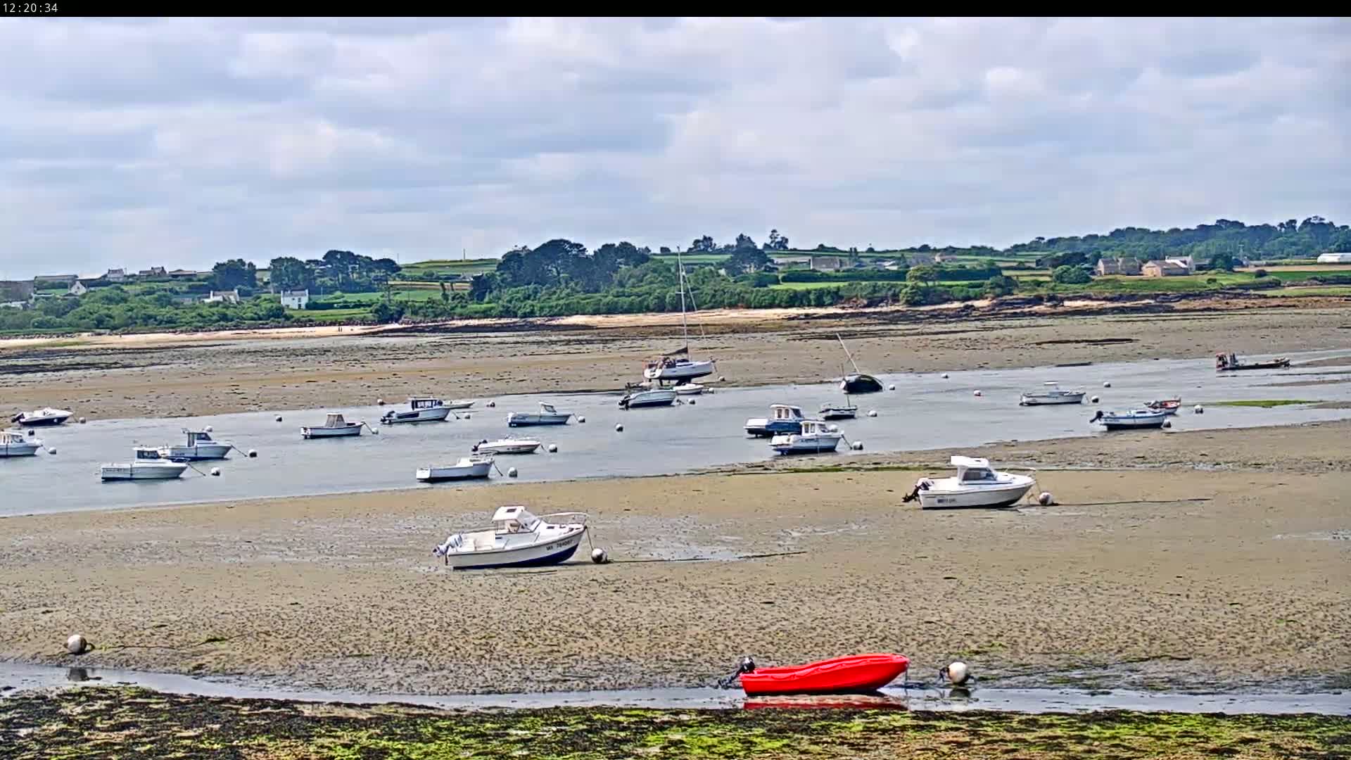 Many small boats are grounded on a wide, sandy tidal flat under a partly cloudy sky.