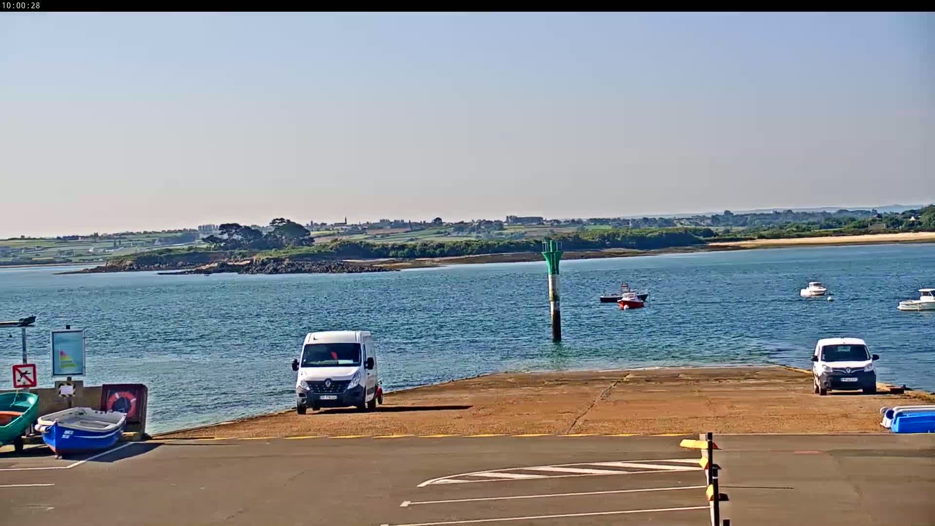 A calm body of water with a few small boats and two white vans parked on a boat ramp, under a clear sky.