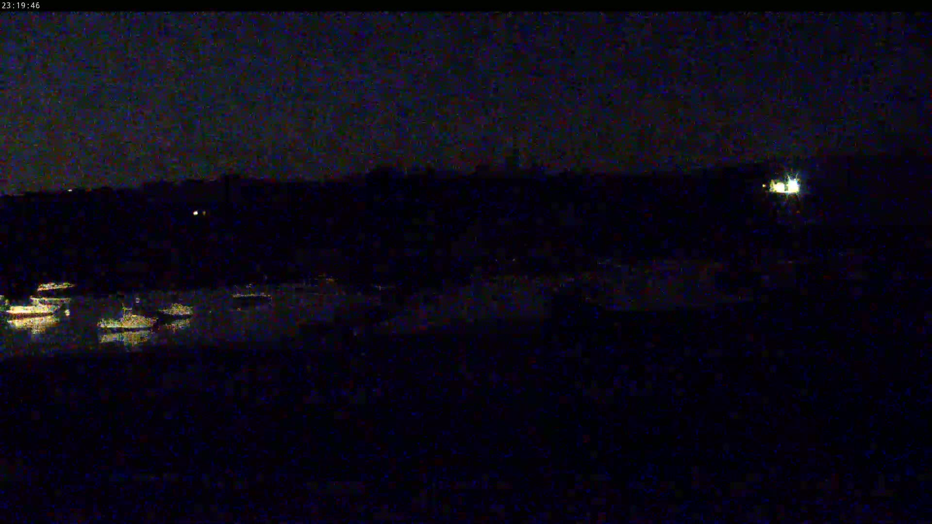 A nighttime, low-light view shows a dark body of water reflecting faint lights from the shore and a few distant lights on land.