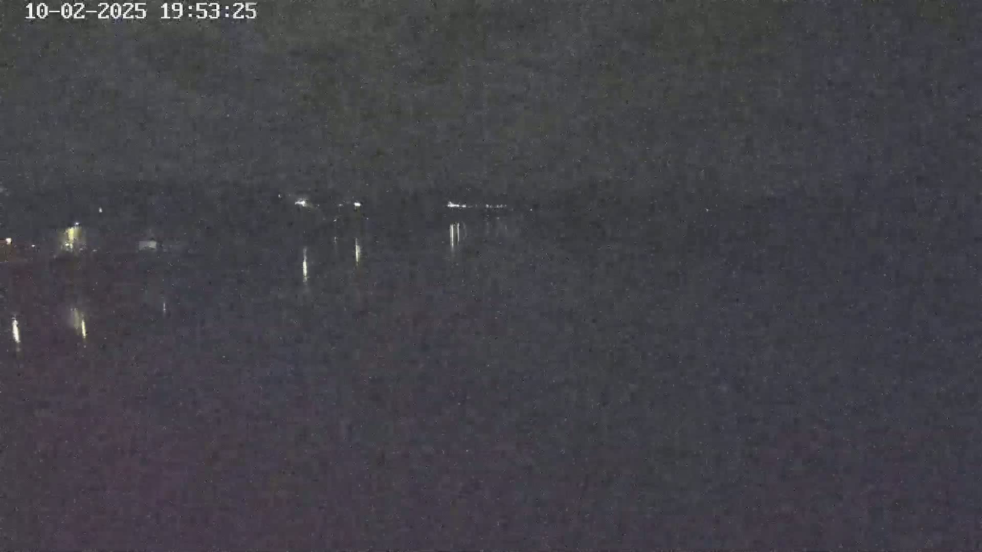 A nighttime view of a dark body of water reflecting distant lights under a clear sky.