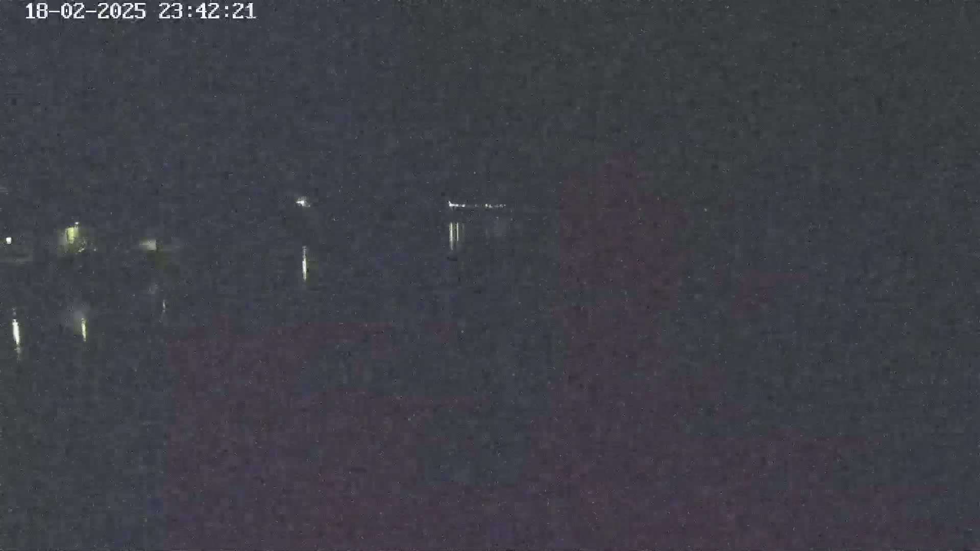 A low-light nighttime image shows several faint lights in the distance, possibly from buildings or vehicles, against a dark, mostly featureless background.