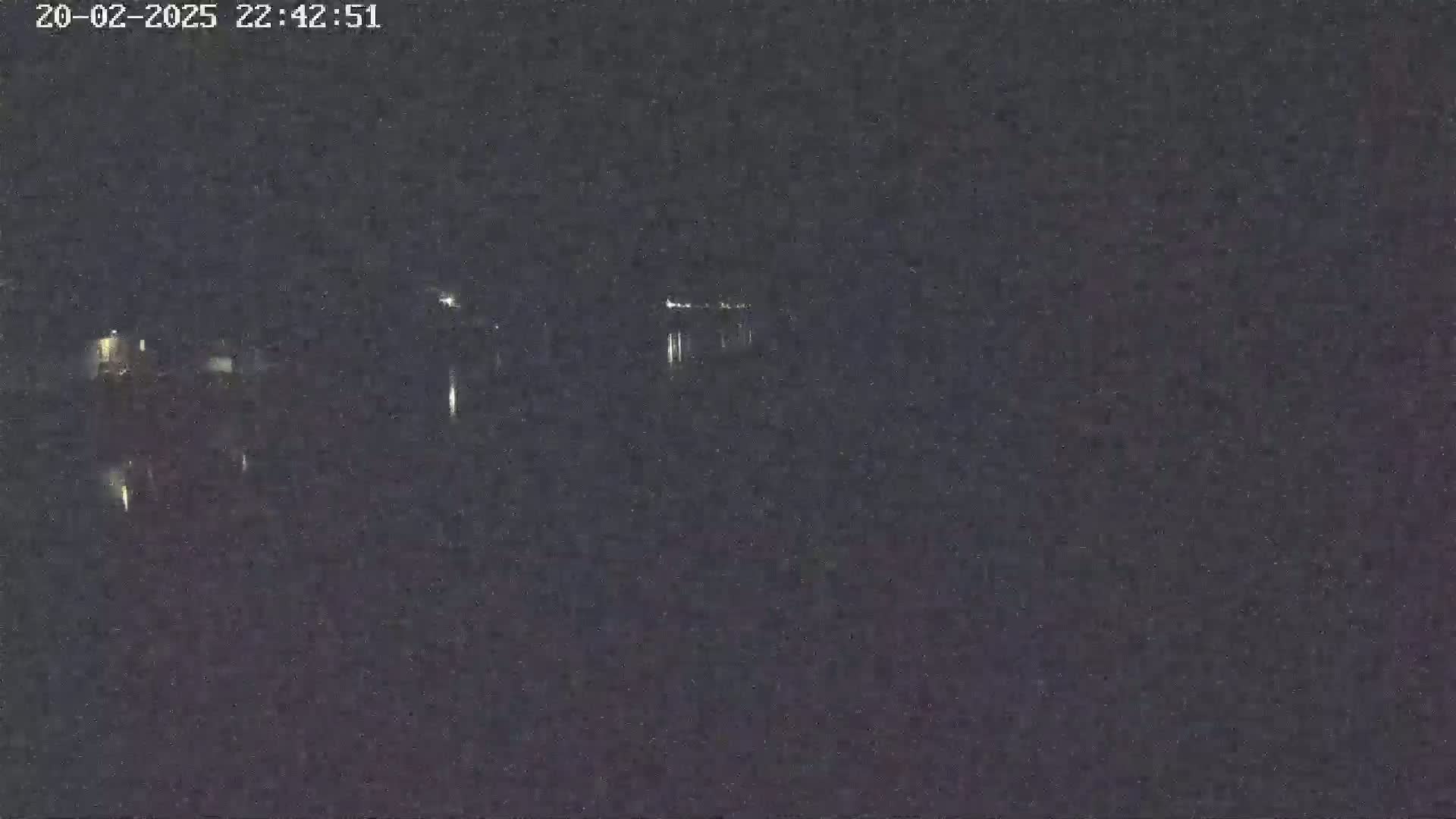 A nighttime, low-light image shows a dark, possibly waterfront area with faint lights visible in the distance.