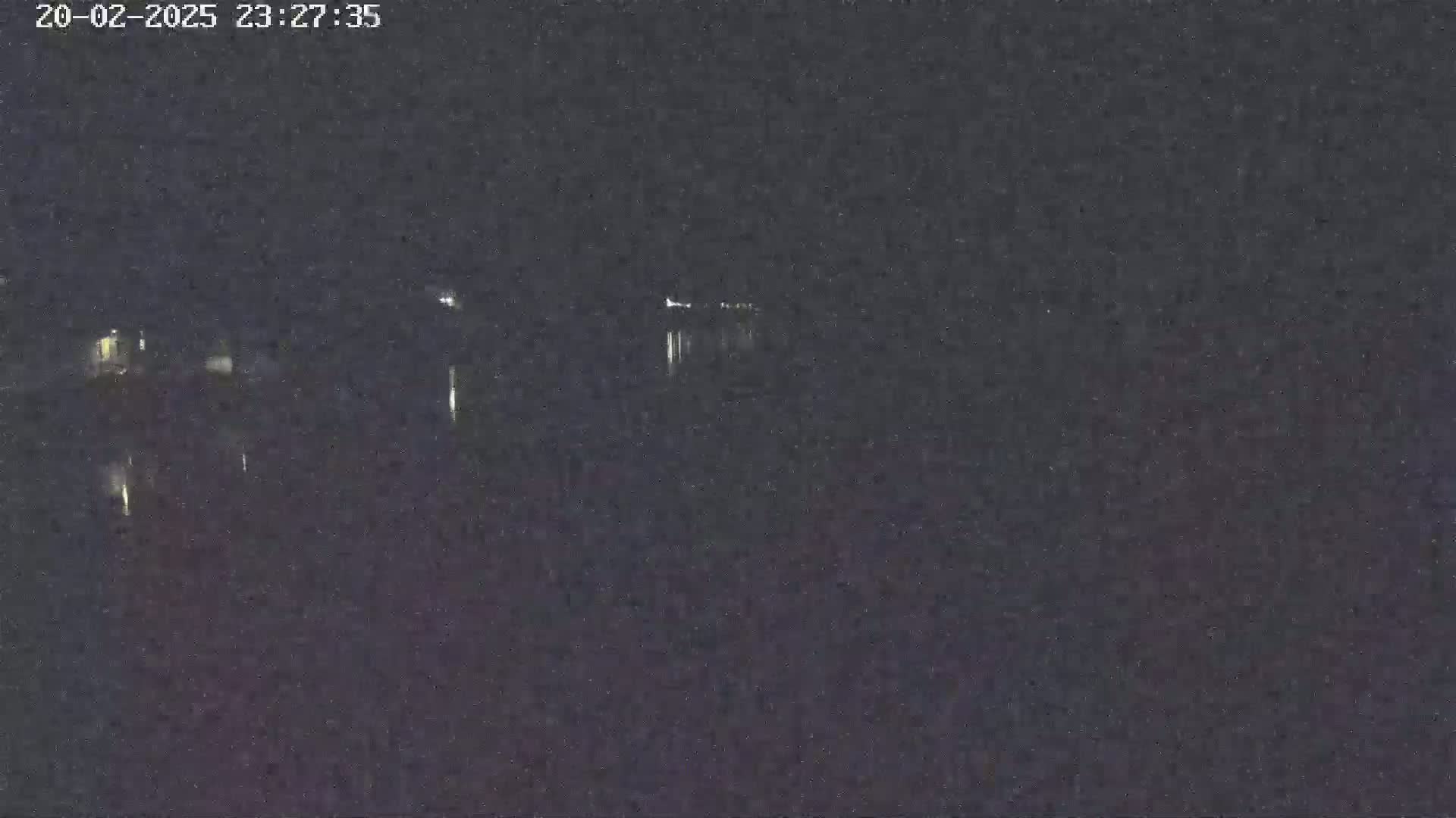 A nighttime, low-light view shows a dark body of water reflecting a few distant lights.