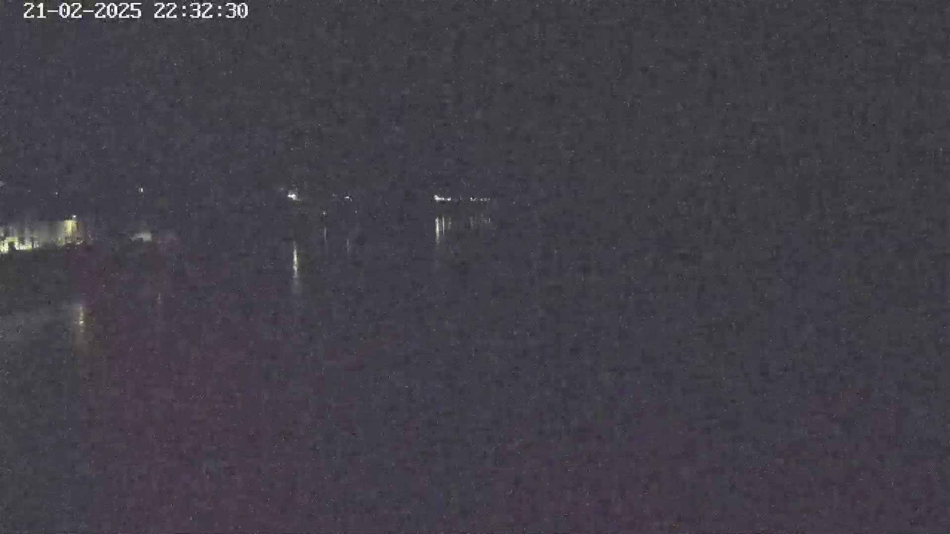 A nighttime, low-light view of a body of water with faint lights visible in the distance on the opposite shore.
