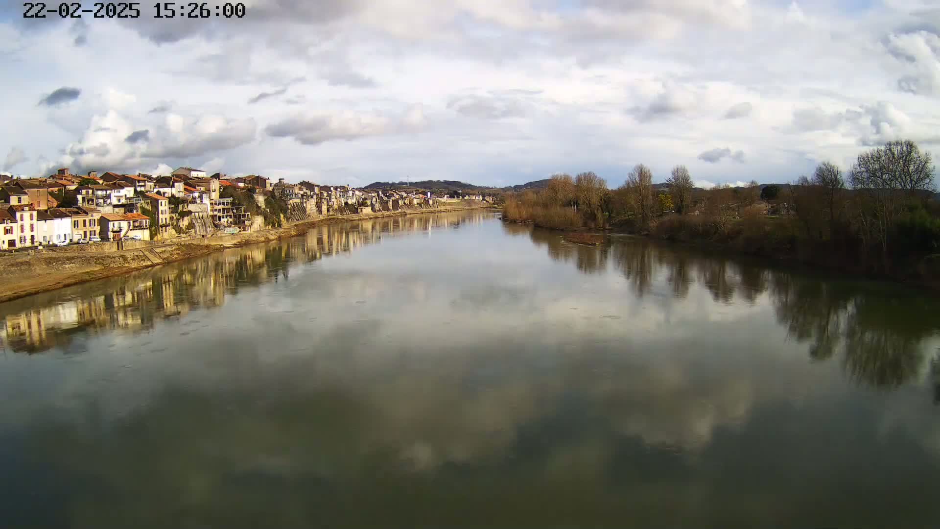 A river reflects a cloudy sky and the buildings of a town on its banks.