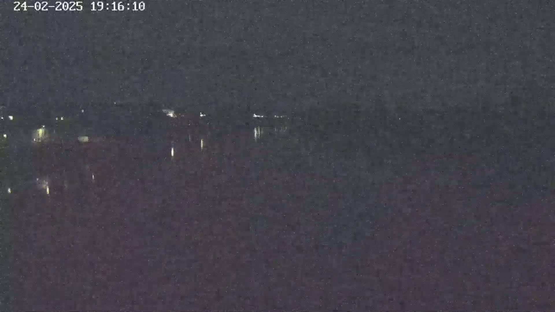 A nighttime long shot shows a dark body of water reflecting a few distant lights under a dark sky.