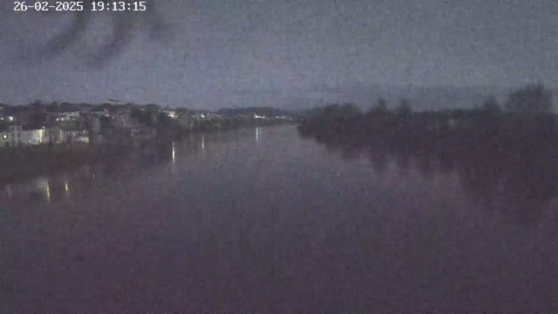A dark, calm river reflects the dim lights of a town under a dusky sky.