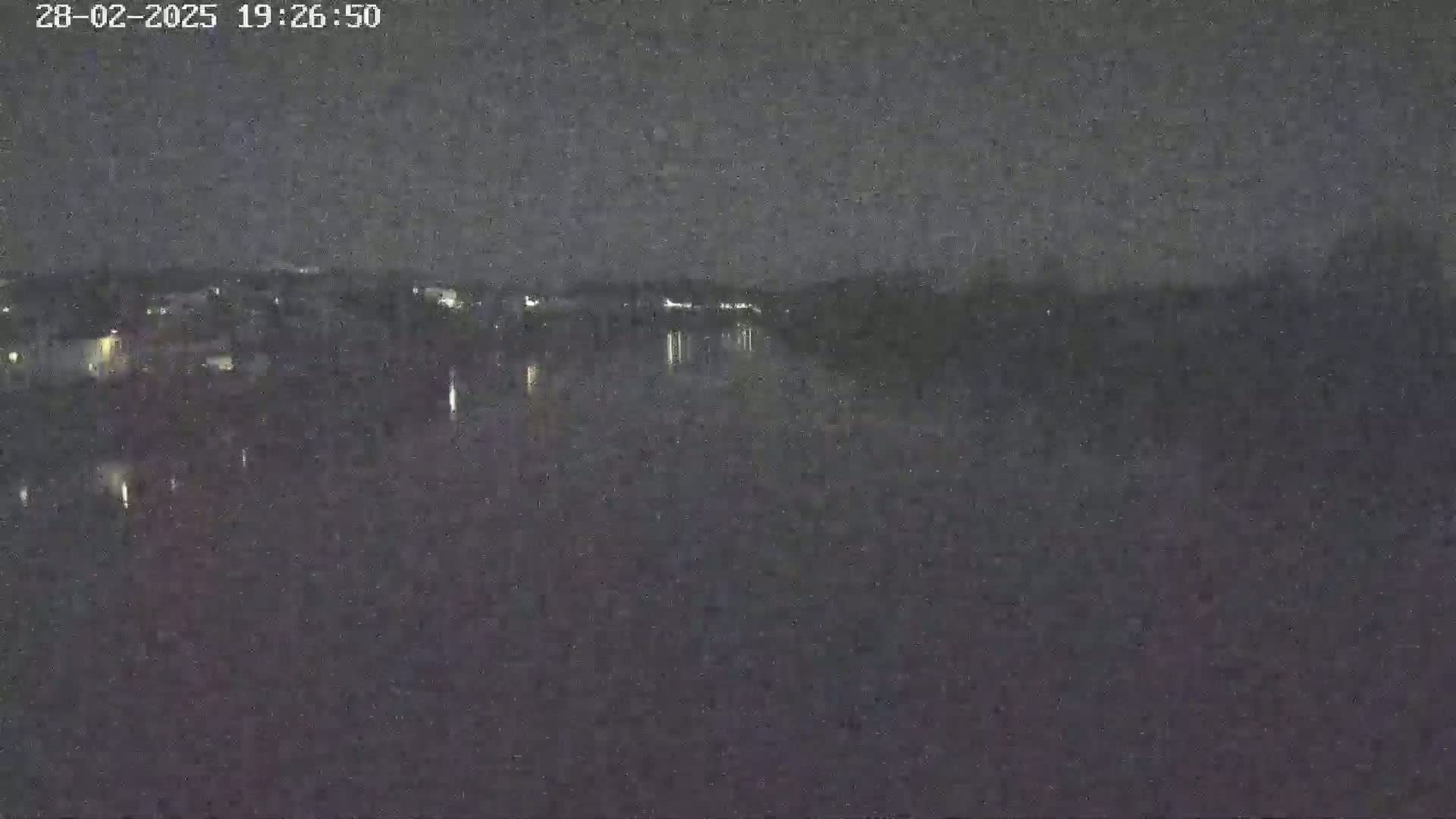 A nighttime view of a dark body of water reflecting faint lights from a distant shoreline under a clear, dark sky.