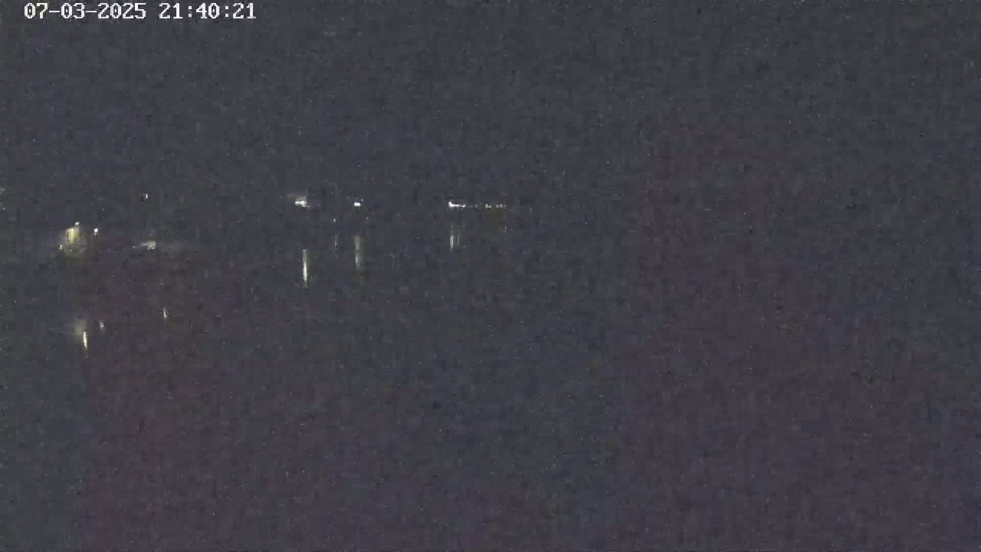 A nighttime long shot shows a dark body of water with faint lights reflecting on its surface from a distant shoreline.