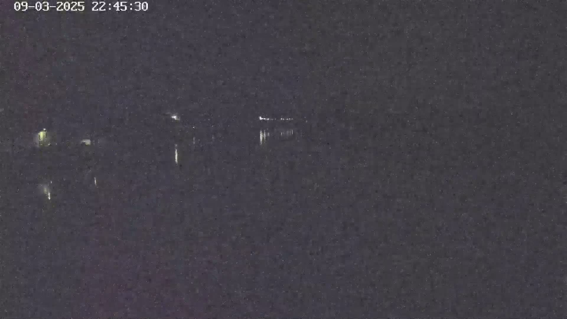 A nighttime, low-light view shows a dark body of water reflecting faint lights from a distant shoreline.