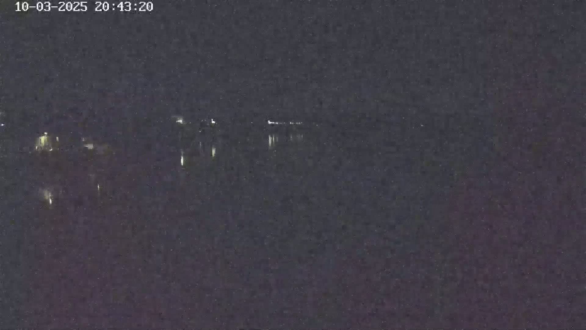 A nighttime view of a dark body of water reflecting faint lights from a distant shoreline under a clear, dark sky.