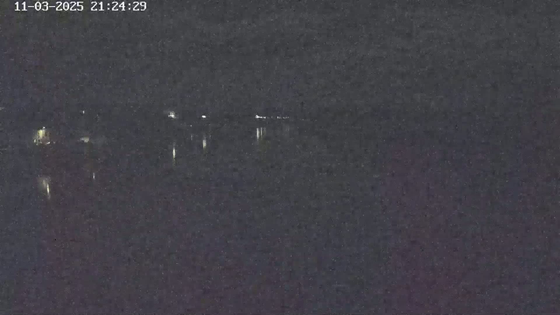 A dark, nighttime view of a body of water reflecting distant lights under a clear sky.