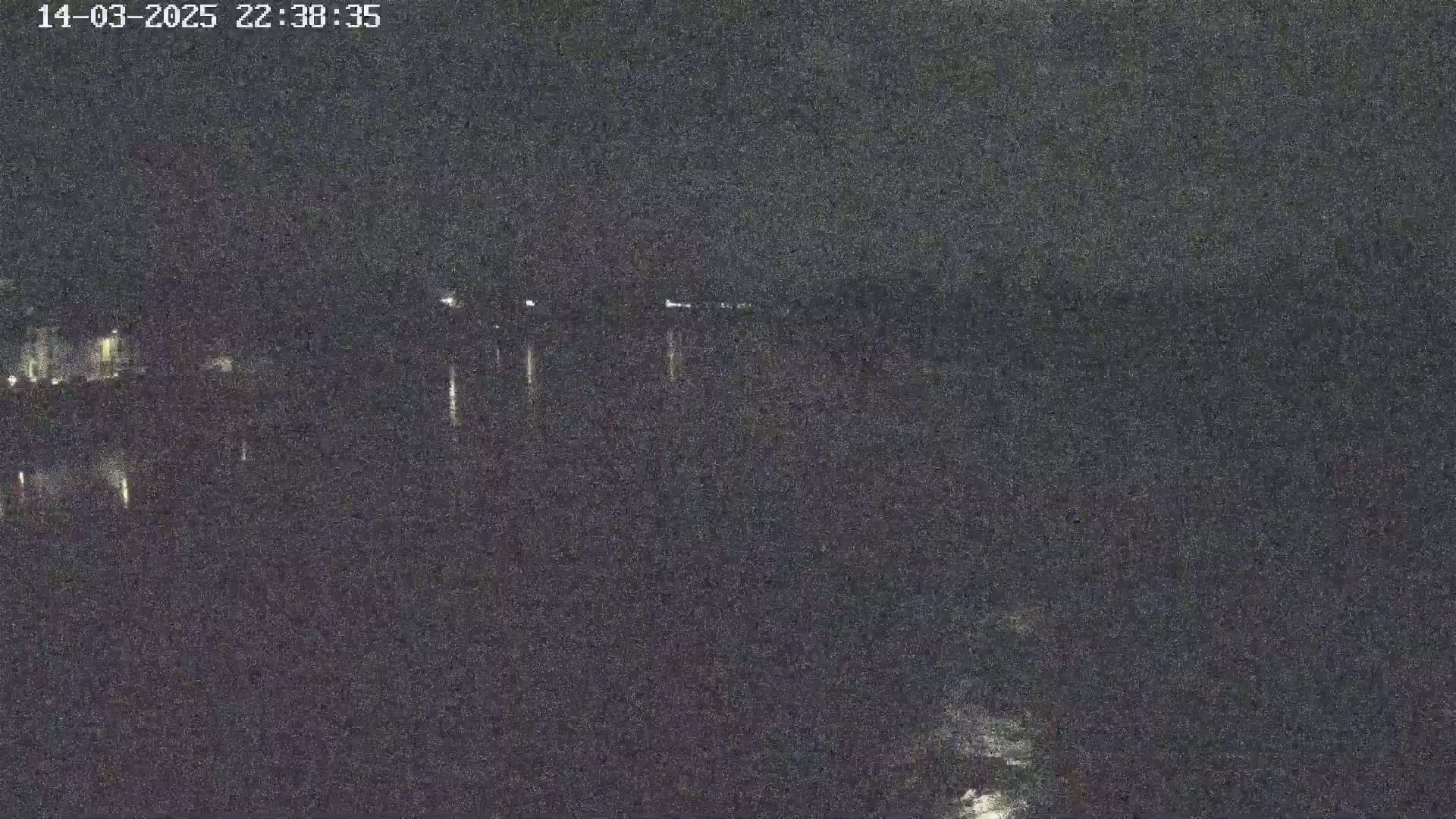 A dark, nighttime scene shows a body of water with faintly visible lights in the distance.