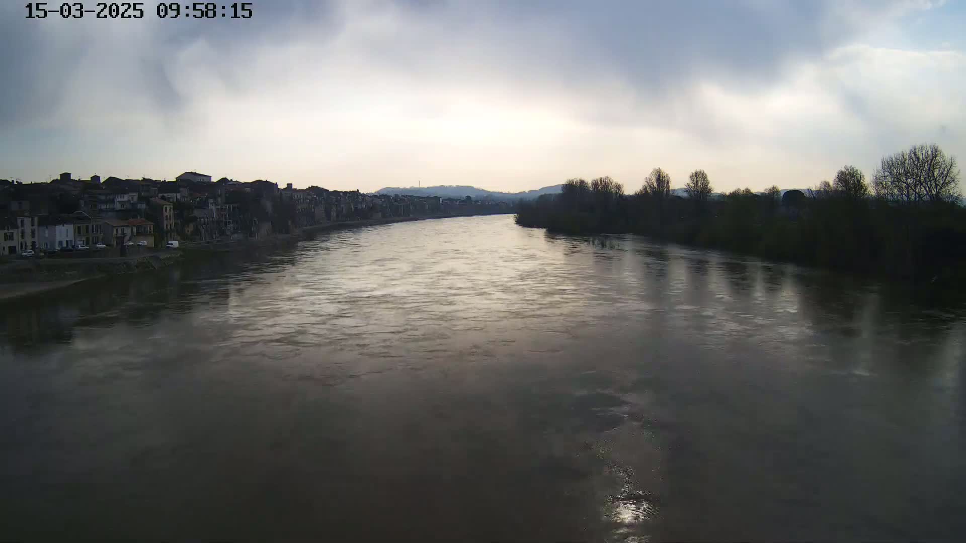A wide, calm river flows past a town under an overcast sky.
