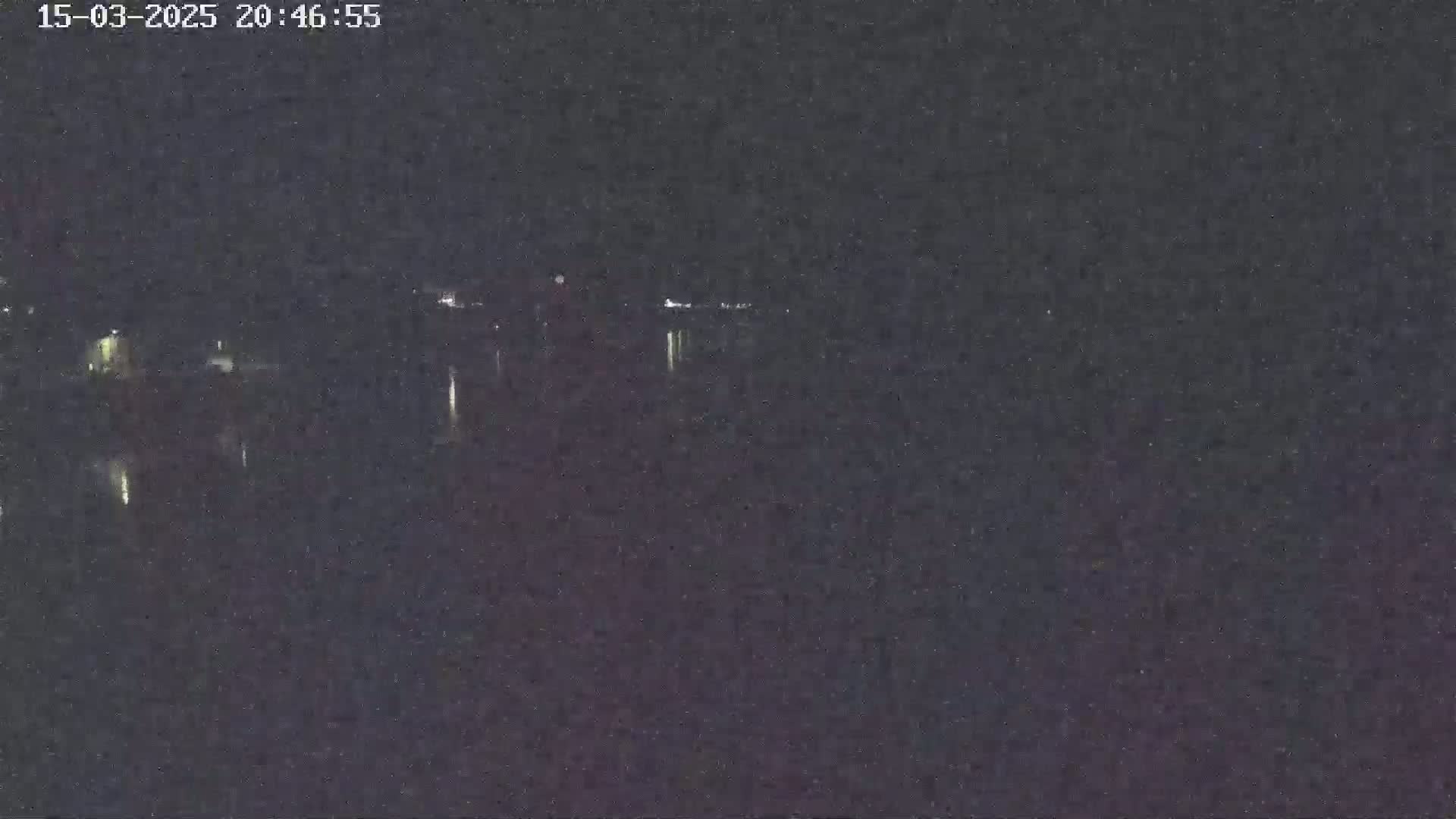 A nighttime, low-light view shows a dark body of water reflecting a few distant lights.