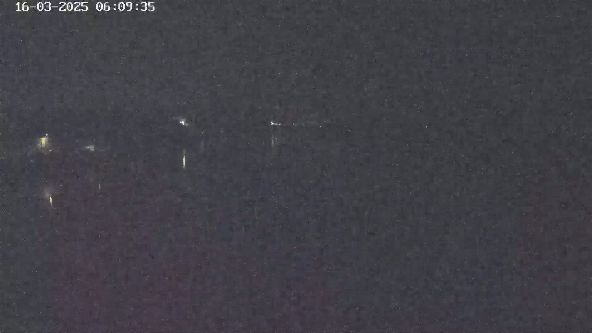 A dark, nighttime image shows a blurry view of distant lights across a body of water under a clear, dark sky.