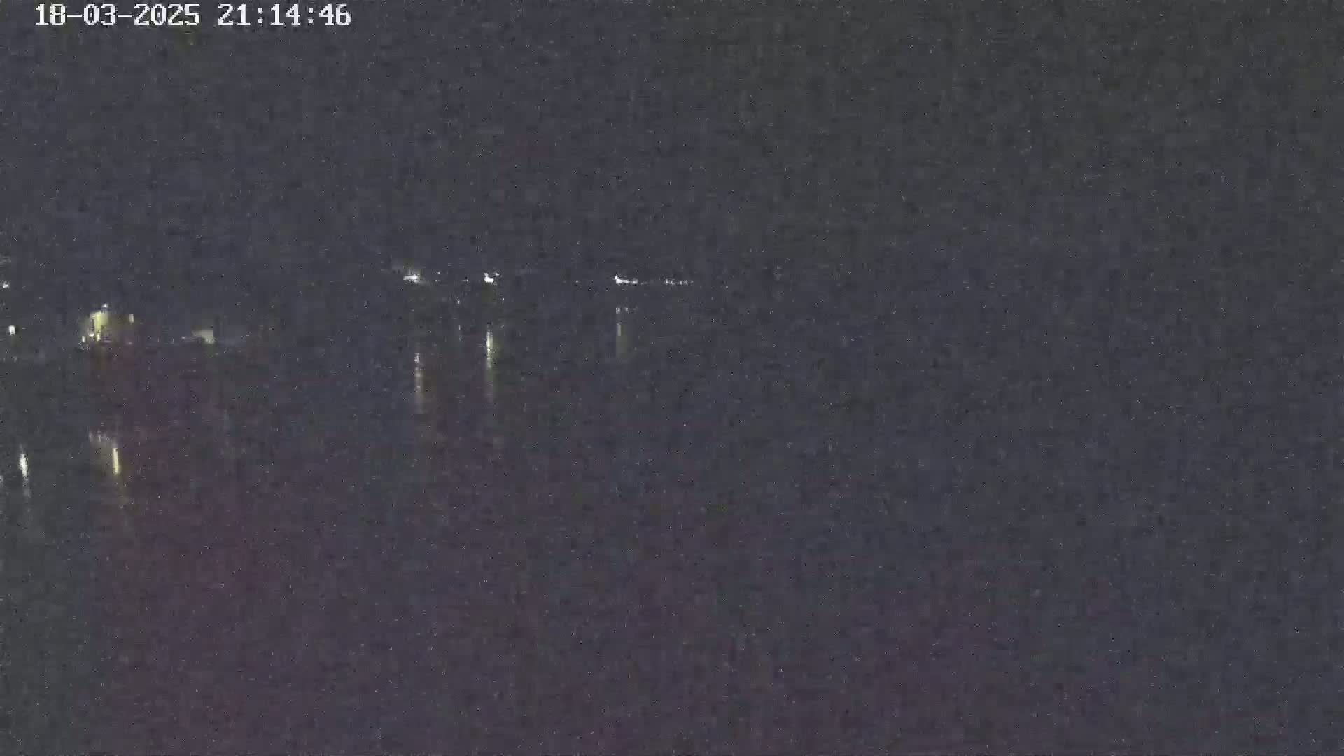 A dark, nighttime image shows a body of water reflecting distant lights under a clear sky.