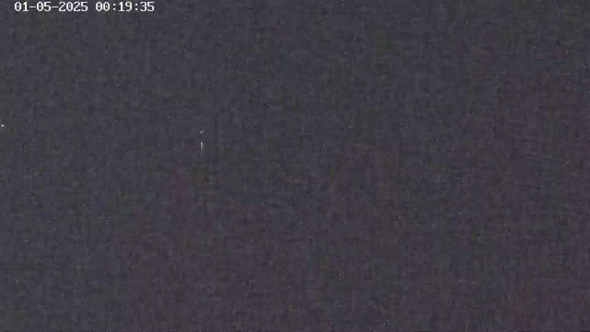 A dark, grainy nighttime image shows a mostly featureless scene with a few faint lights in the distance.