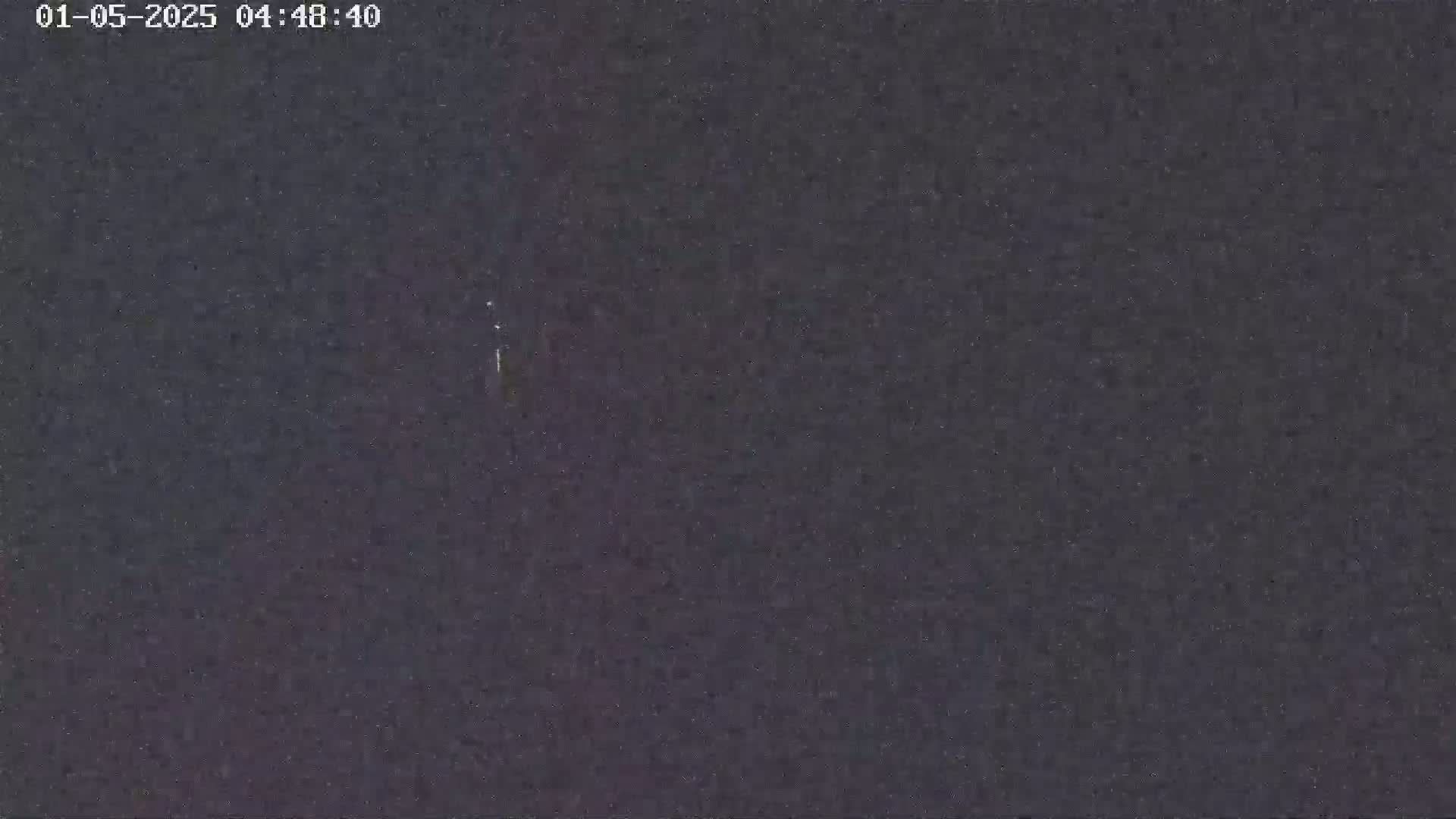 A dark, grainy image shows a mostly clear night sky with a few faint streaks of light.