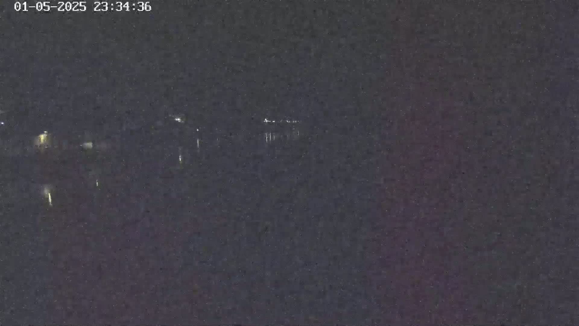 A nighttime long shot shows a dark body of water reflecting a few distant lights under a dark sky.