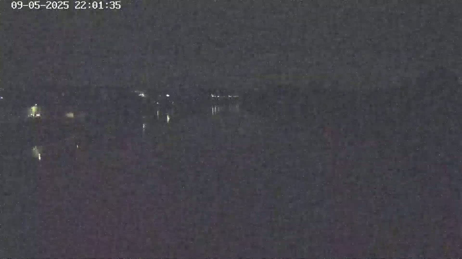 A nighttime view of a dark body of water with faint lights visible on the opposite shore under a clear, dark sky.