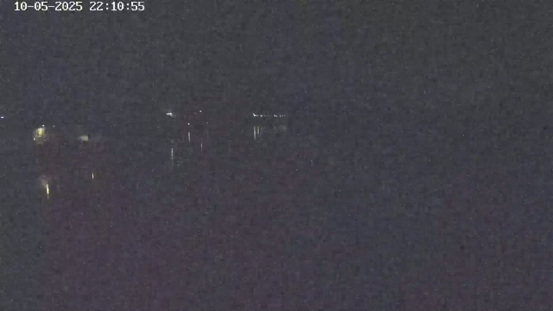 A nighttime, low-light view shows a dark body of water reflecting faint lights from a distant shoreline.