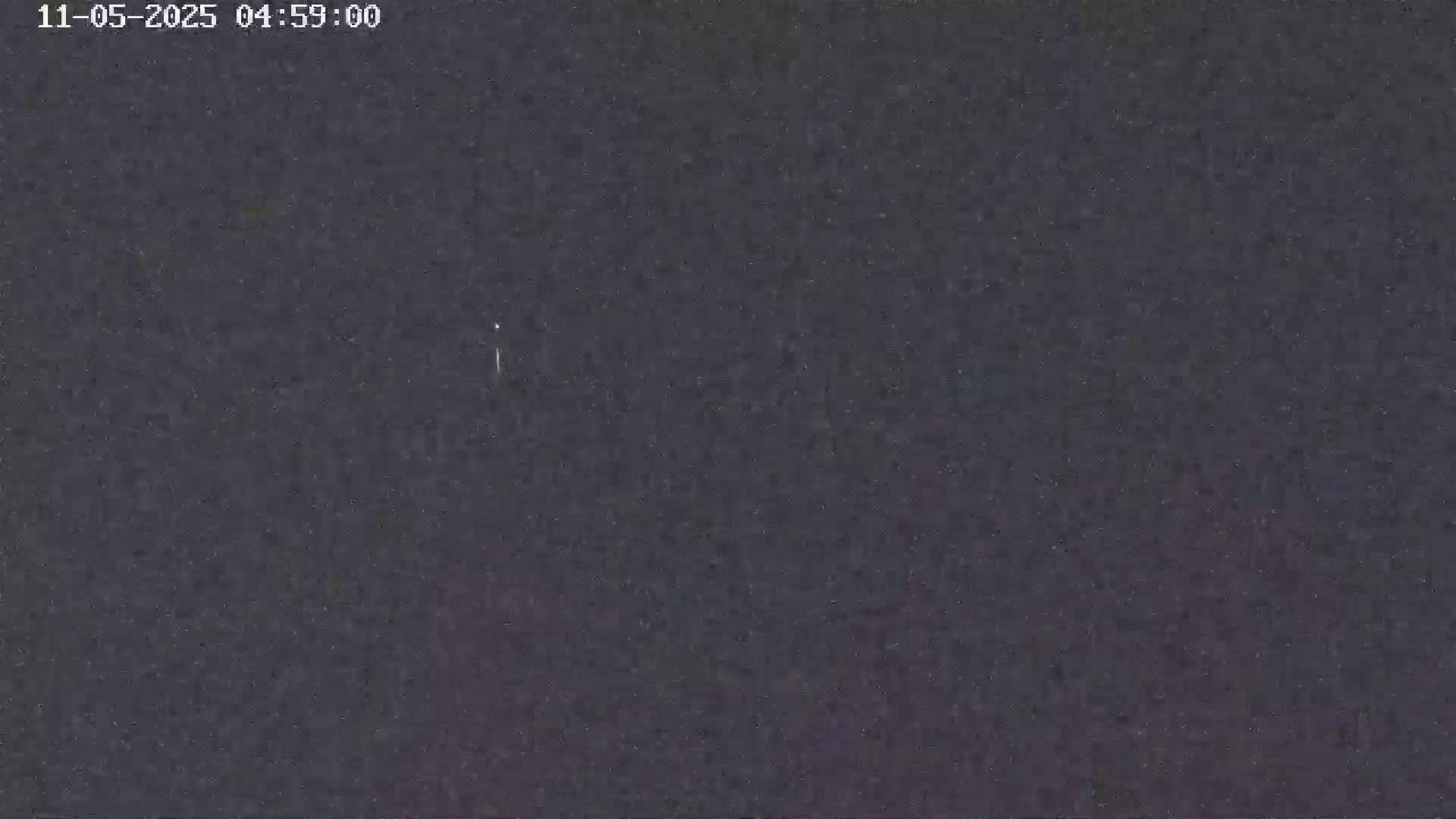 A dark, nighttime scene shows a faint, light streak in the sky.