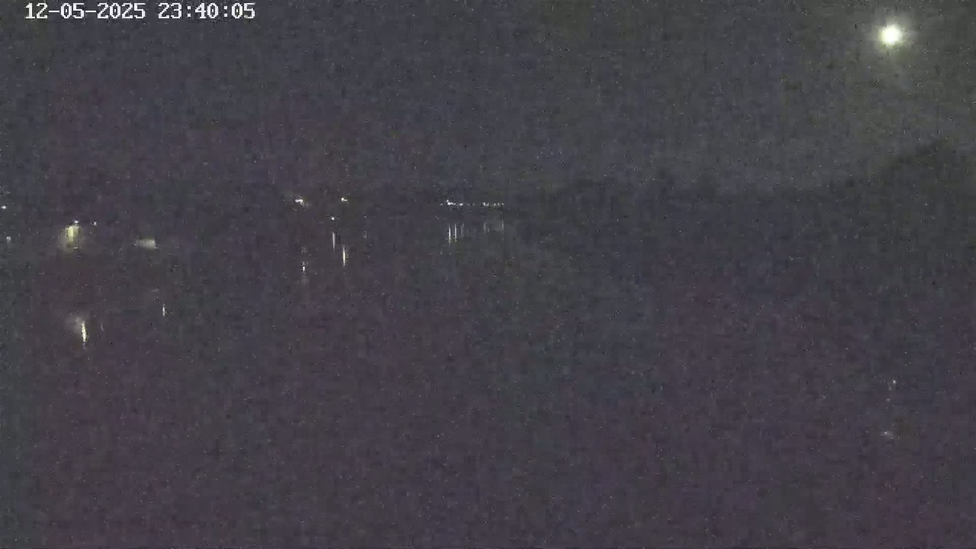A nighttime, low-light view of a body of water with faint lights on the far shore under a moonlit sky.