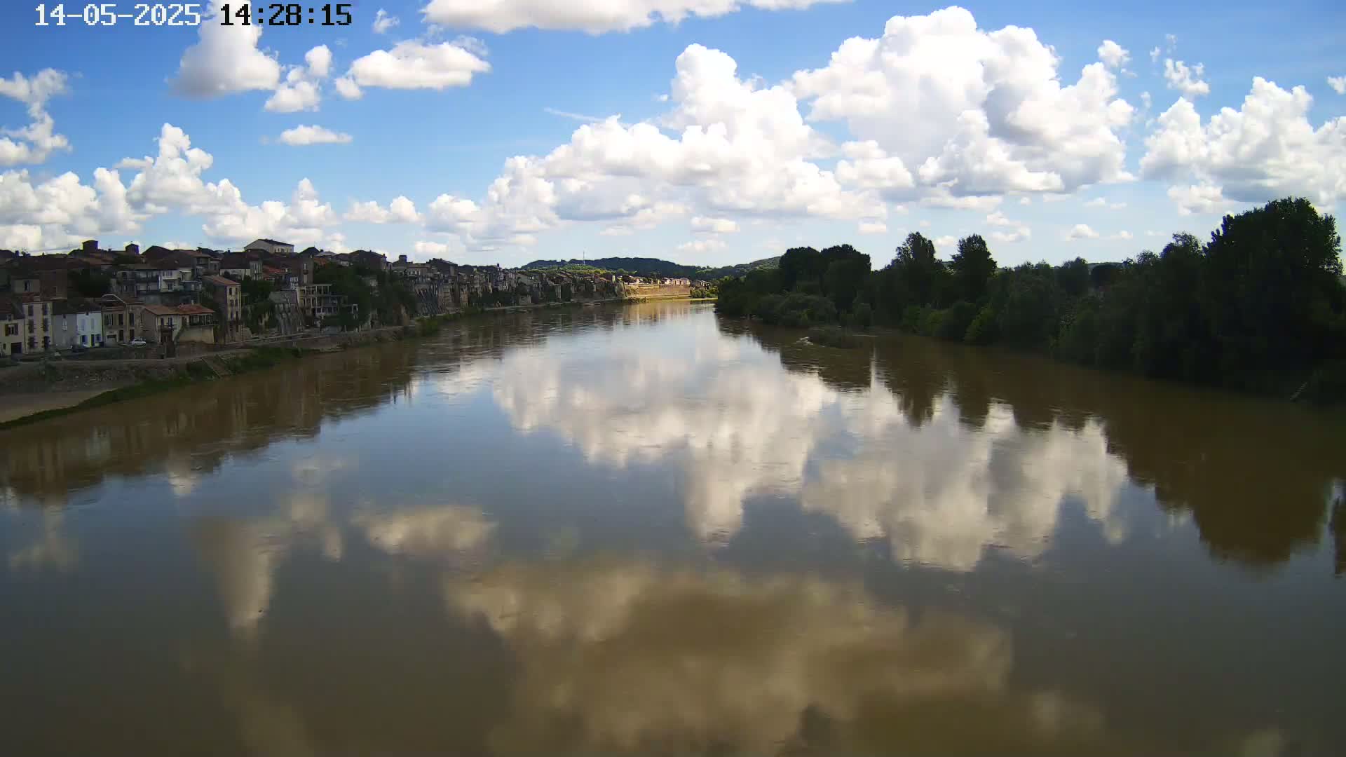 A river reflects a partly cloudy sky and a town on its banks.