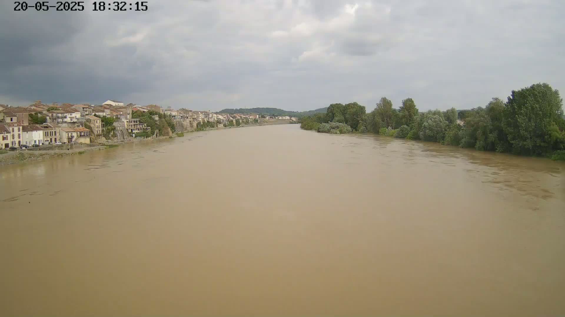 A wide, muddy river flows past a town under an overcast sky.