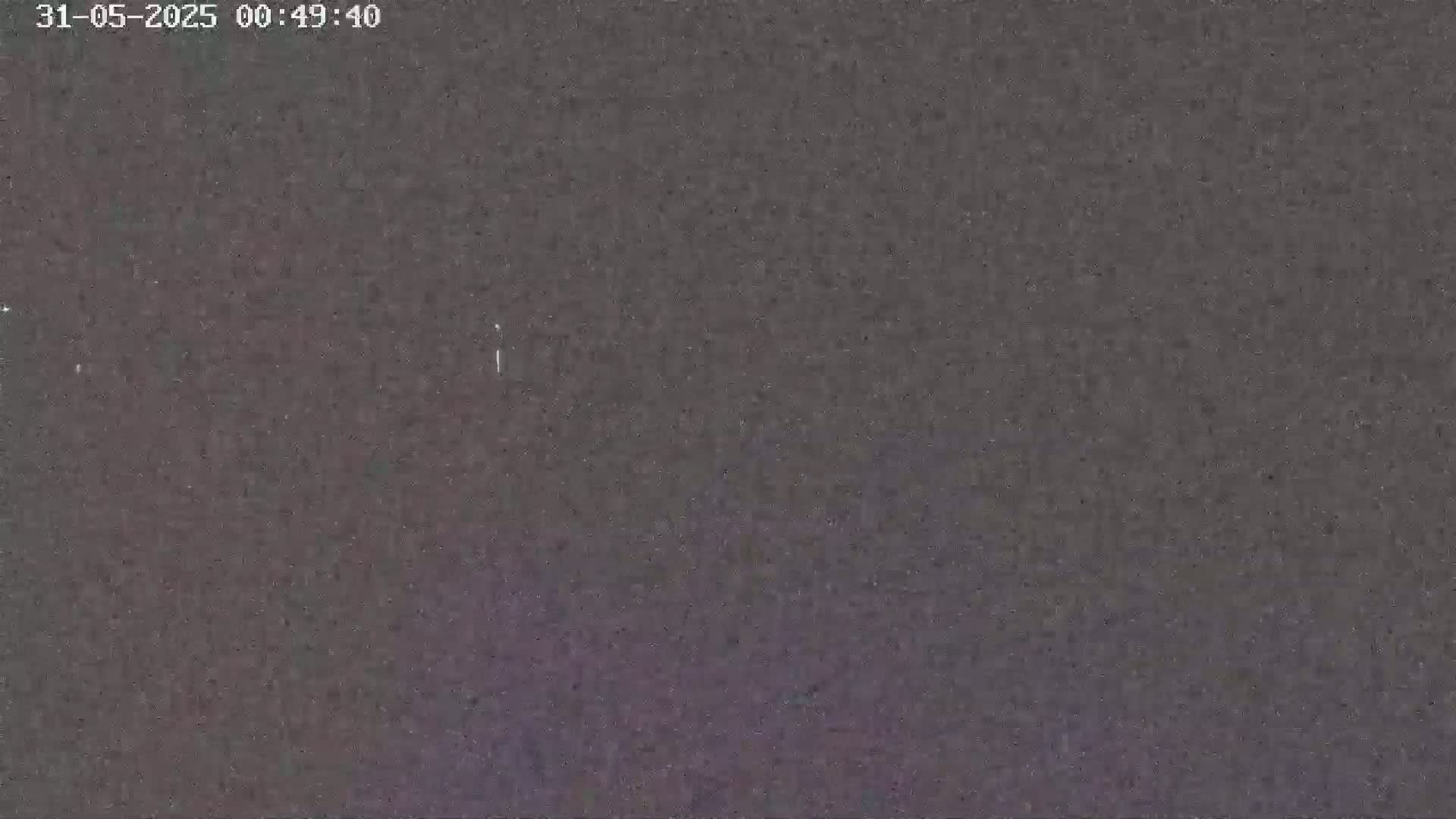 A dark, grainy image shows a mostly clear night sky with a few faint lights visible.