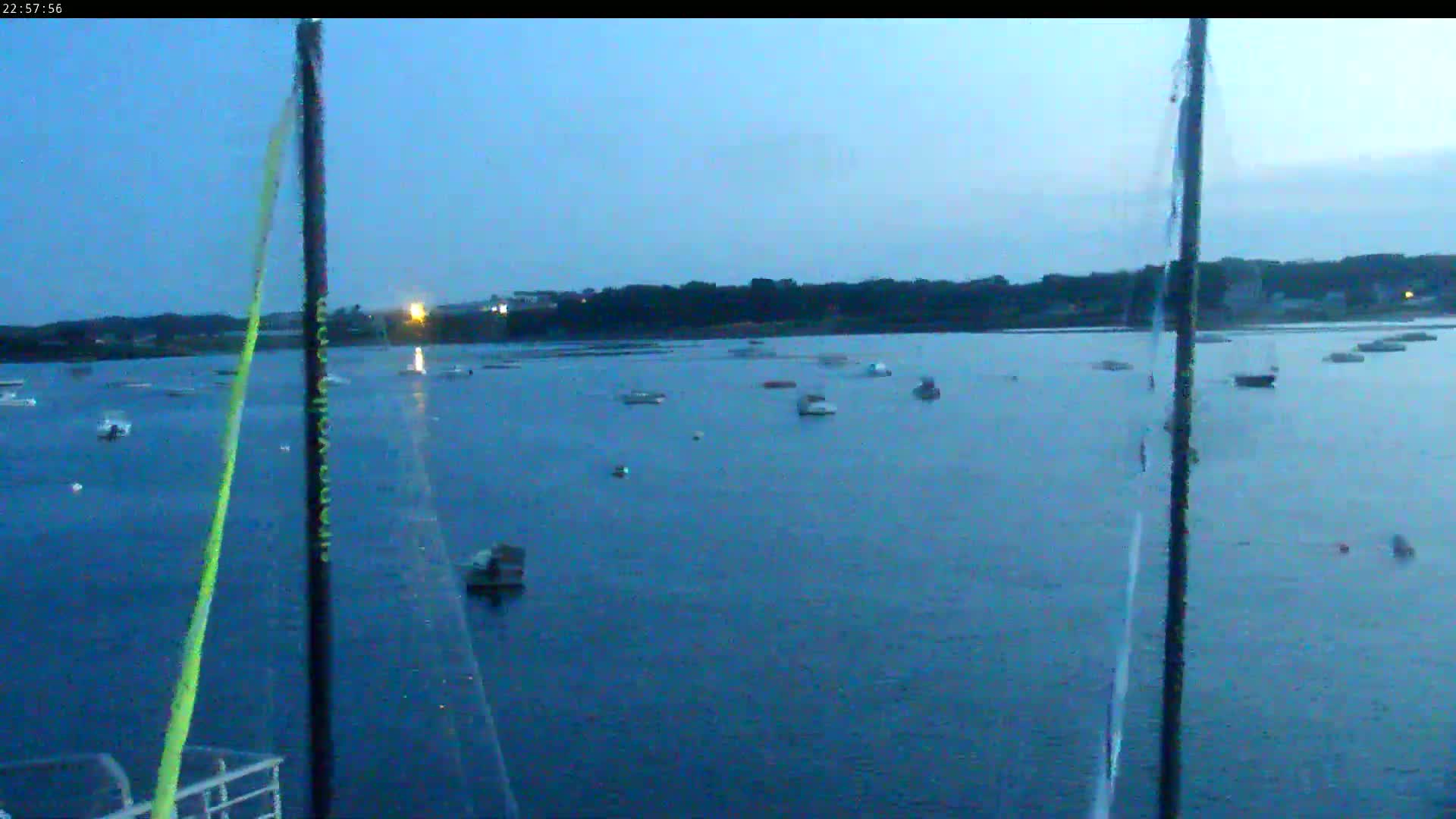 Several boats are moored in a calm body of water at dusk, with a dark shoreline visible in the distance.