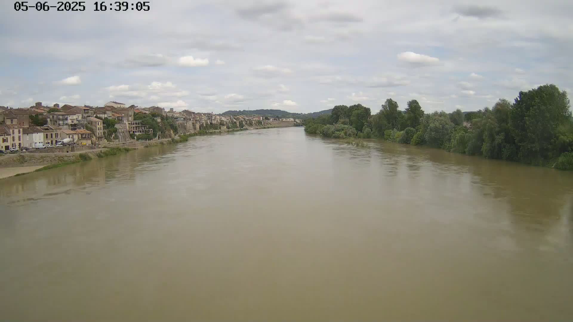 A wide, muddy river flows past a town under a cloudy sky.