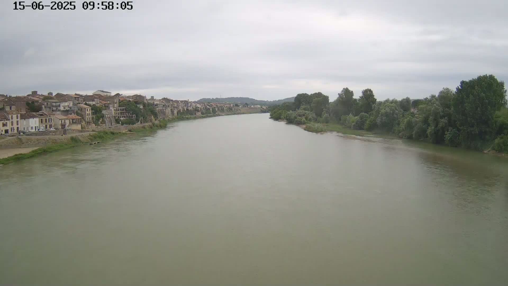 A wide, murky river flows past a town under a cloudy sky.