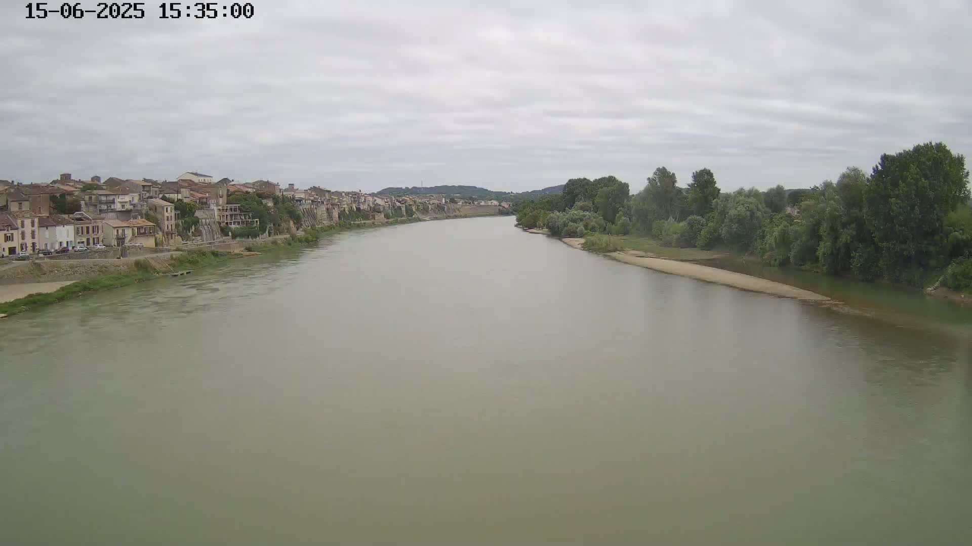 A wide, murky river flows past a town of old buildings under a cloudy sky.
