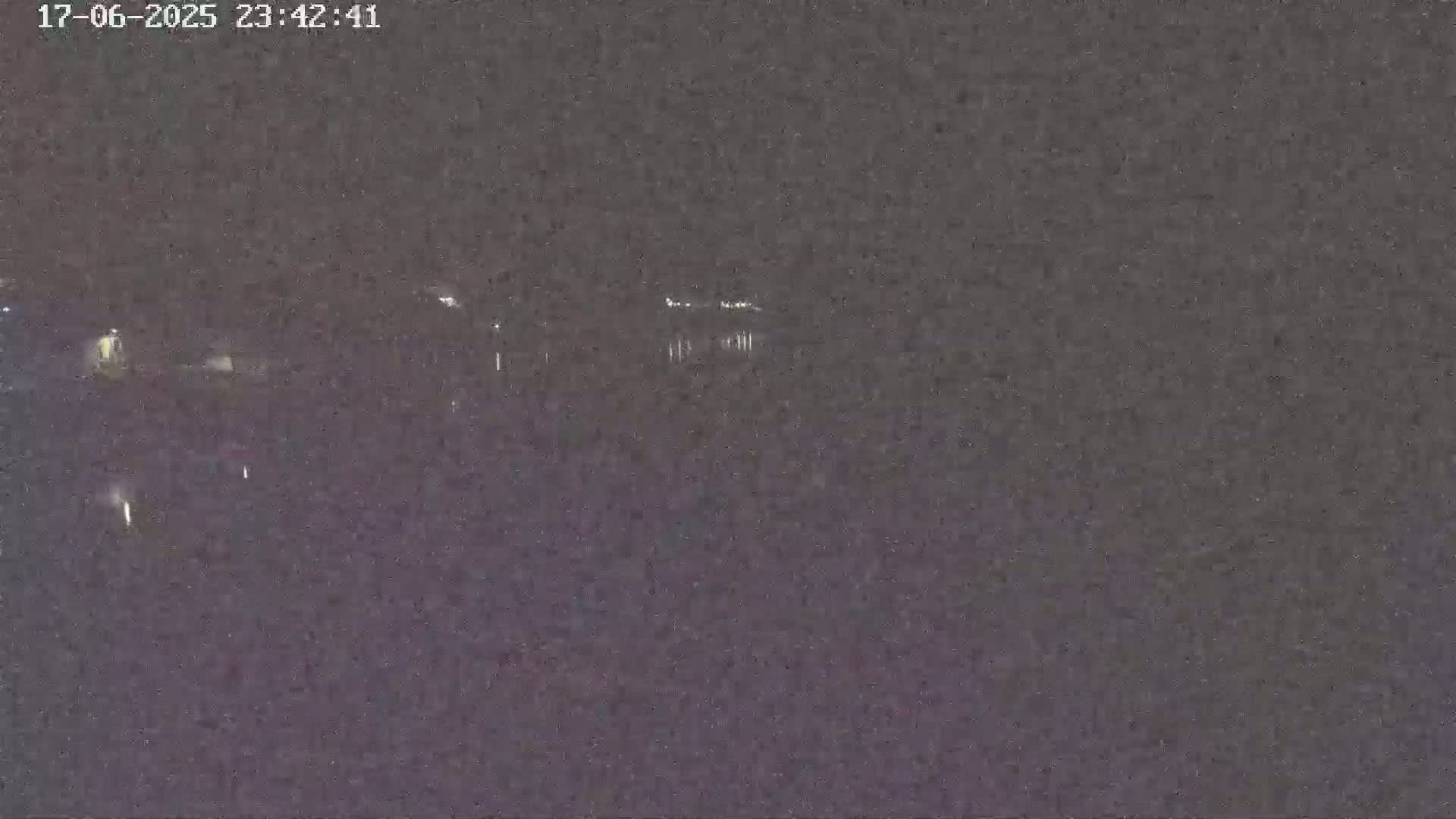 A nighttime, low-light image shows a dark body of water with faintly visible lights in the distance.