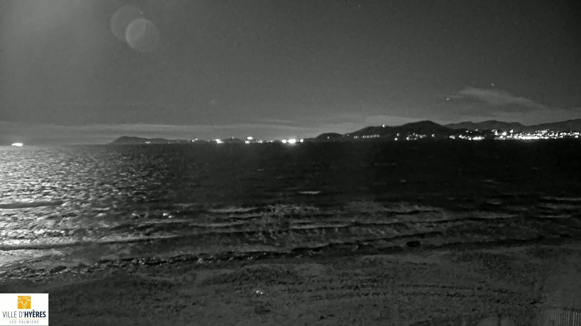 A dark, nighttime beach scene shows gently rolling waves lapping the shore under a mostly clear sky.