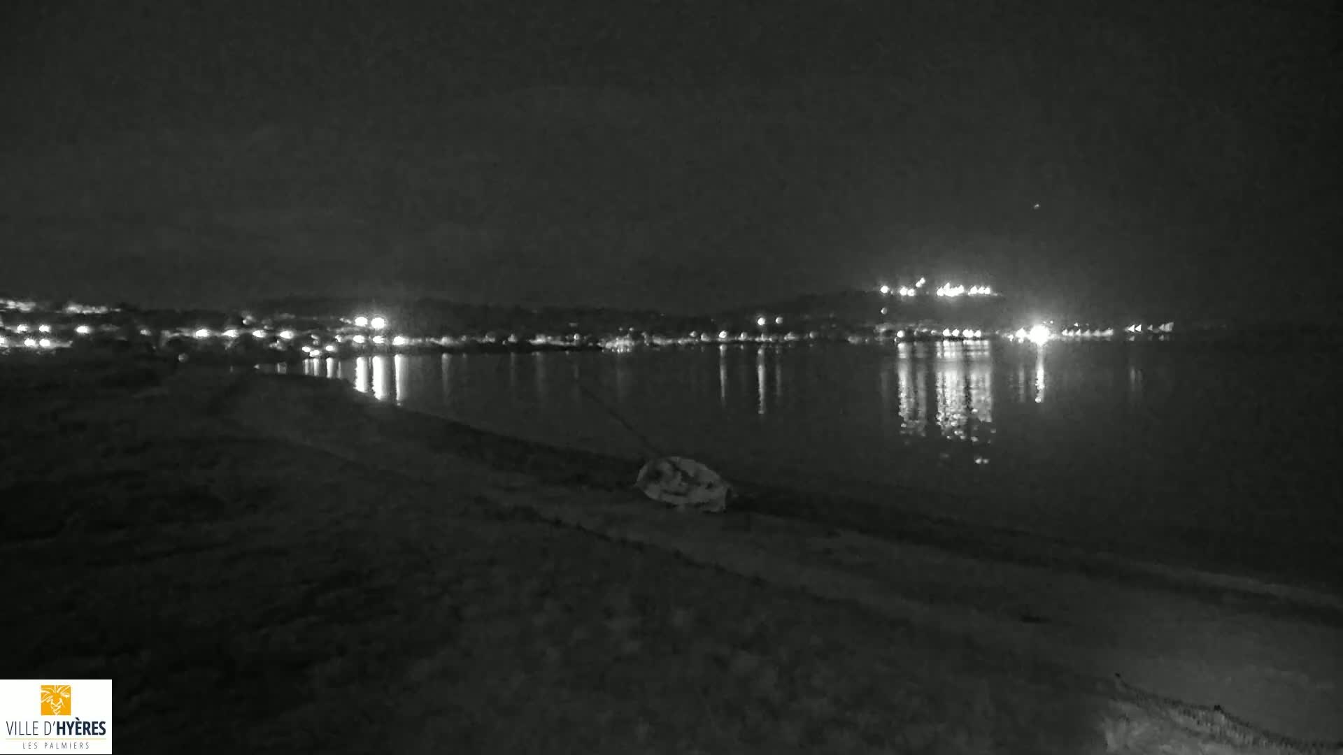 A nighttime view of a calm body of water reflecting the lights of a distant town under a dark sky.
