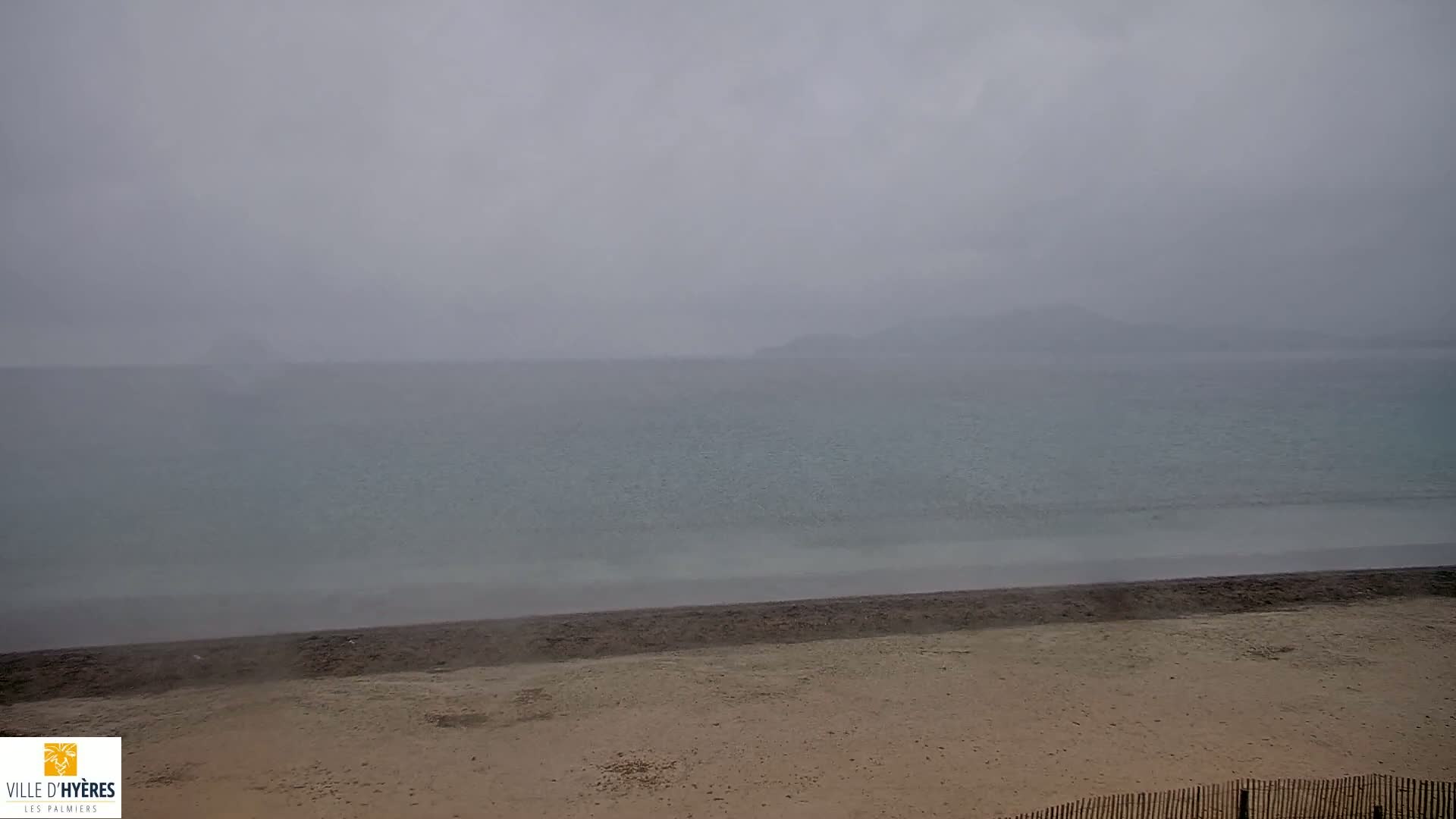 A sandy beach meets a calm, gray-blue sea under an overcast sky.