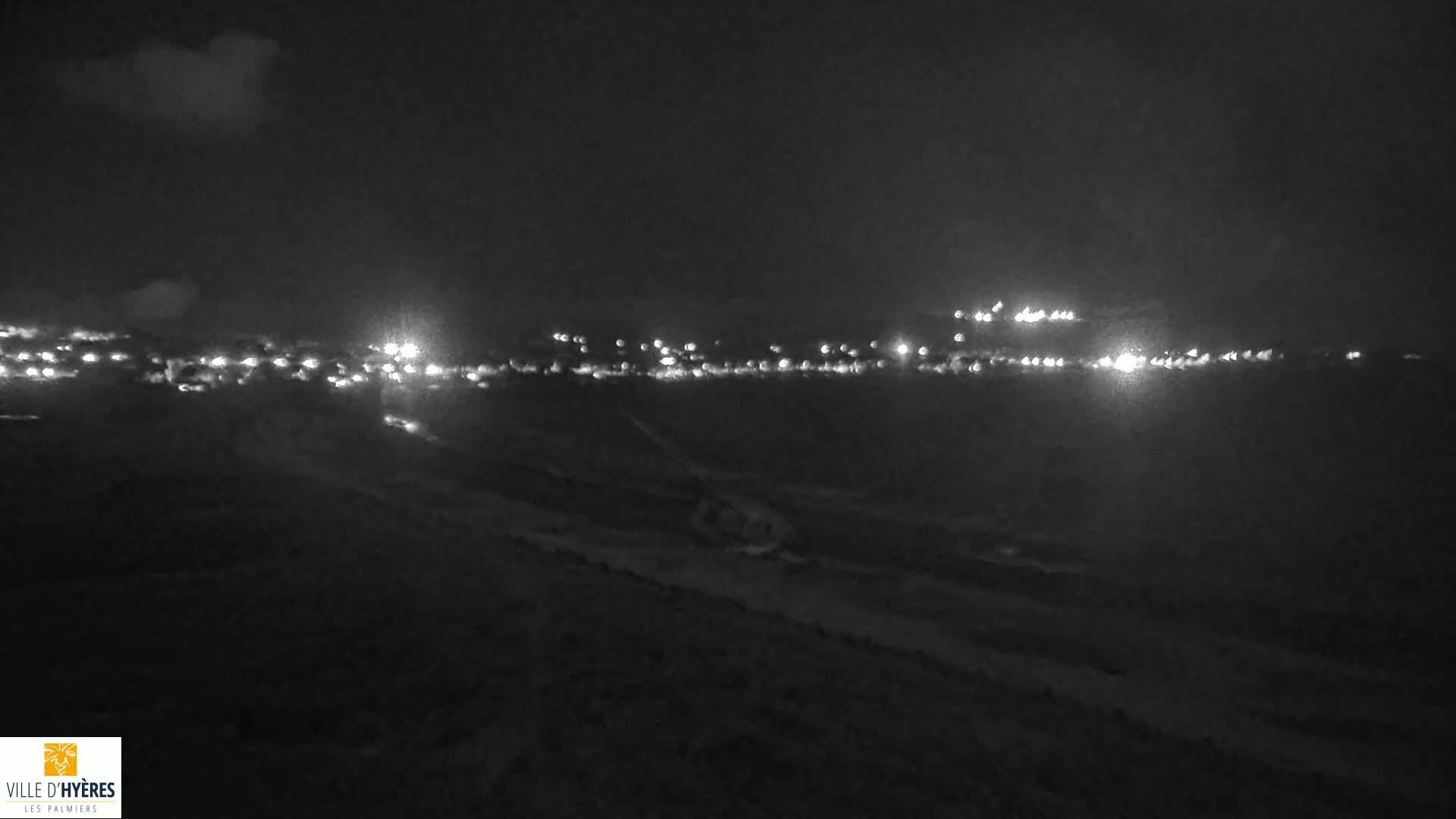 A nighttime, low-light view shows a distant town illuminated by many small lights against a dark sky with some clouds.