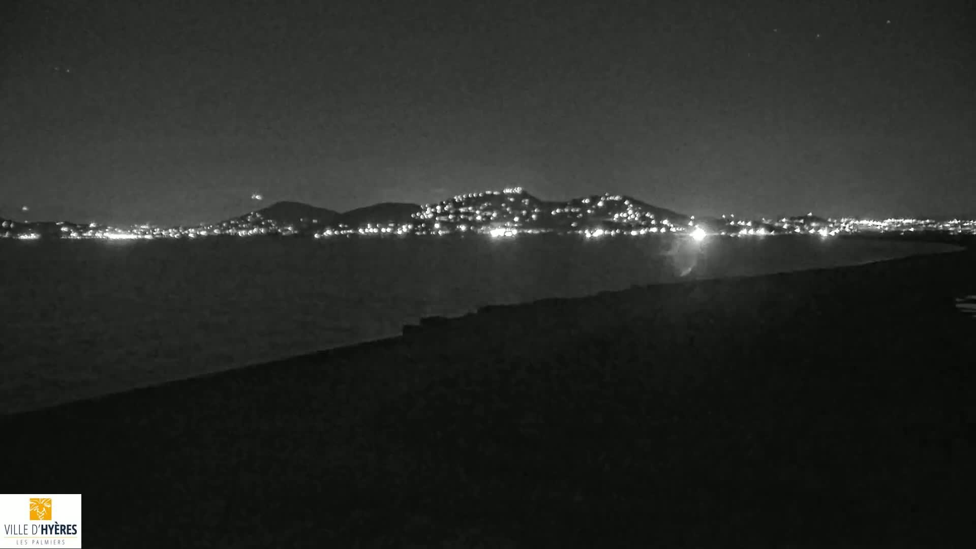 A nighttime view shows a city's lights illuminating a distant hill across a dark body of water.