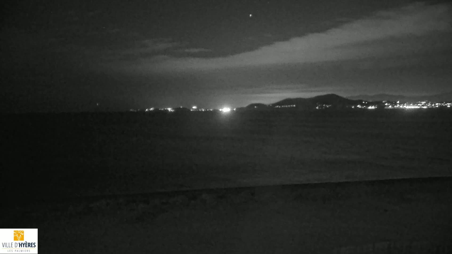 A nighttime, low-light view of a distant city skyline illuminated by lights against a cloudy sky.