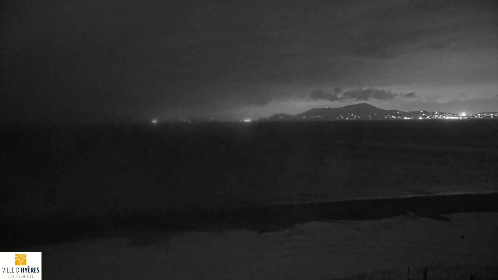 A nighttime, overcast view of a dark body of water with a distant city skyline faintly illuminated.
