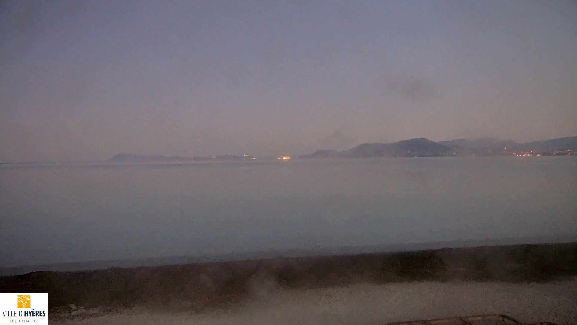 A hazy, low-lying fog obscures a body of water and distant mountains at twilight.