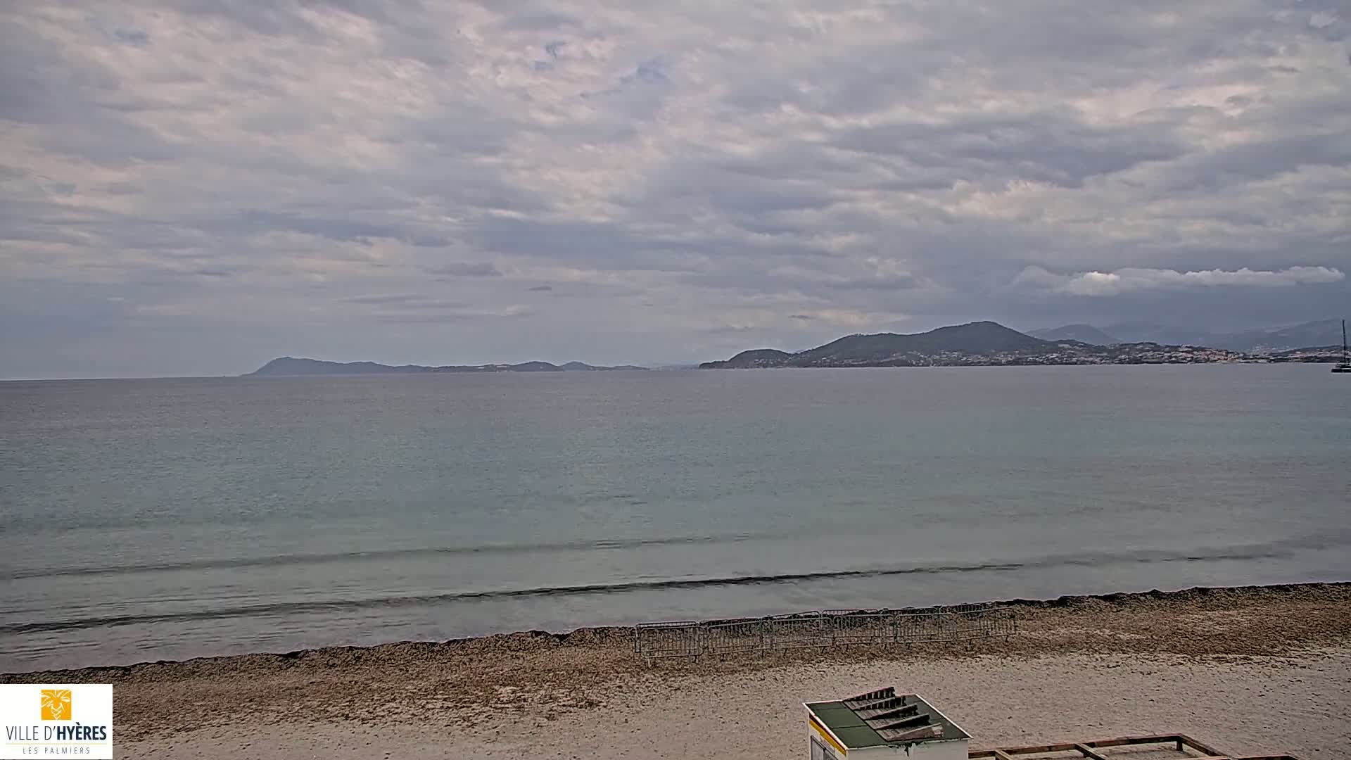 A sandy beach with a calm sea and distant mountains under a cloudy sky.