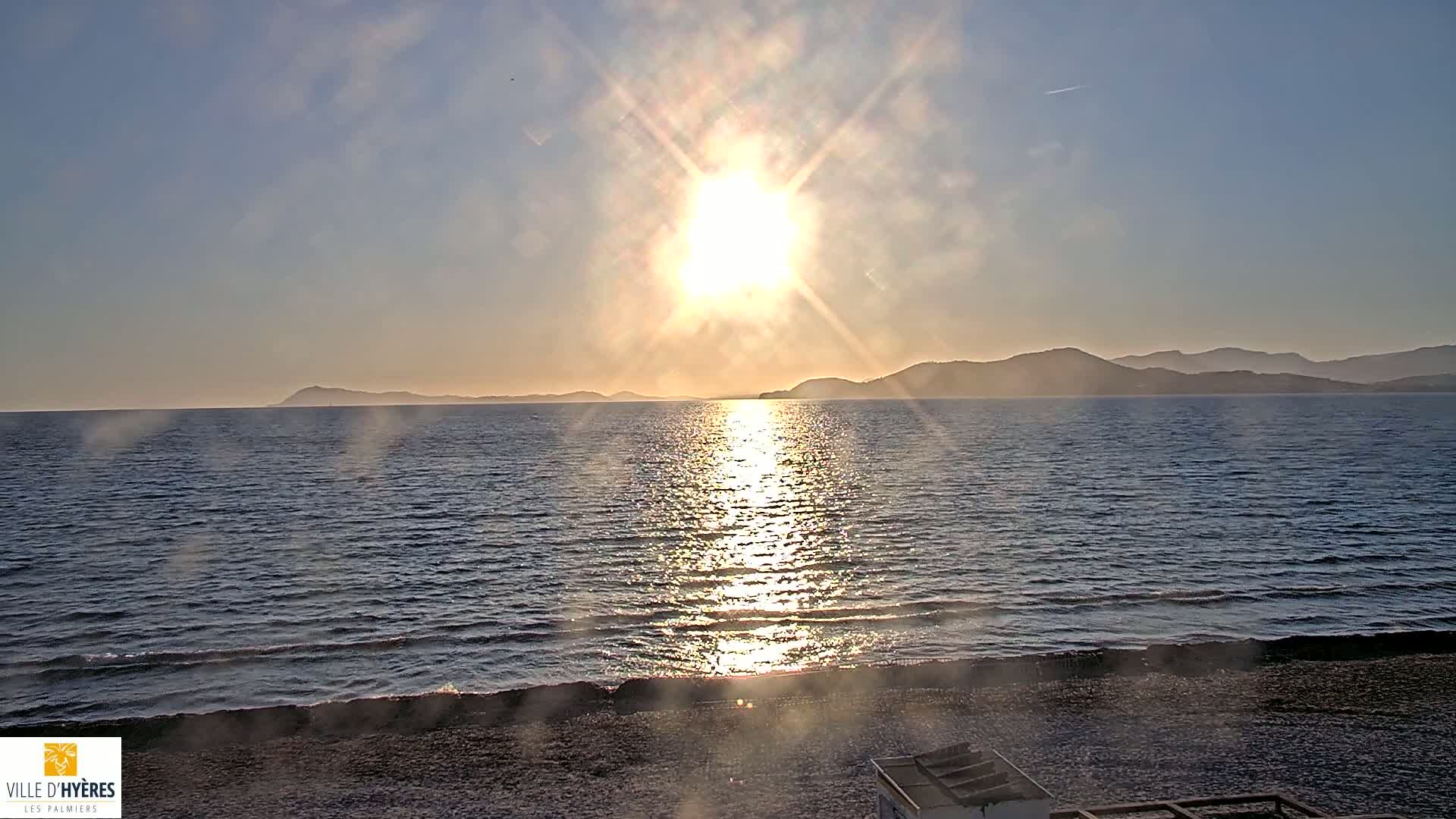 A hazy sunset shines over a calm sea with a distant mountain range.