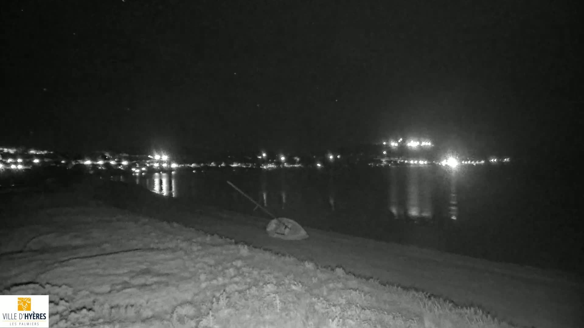 A dark, nighttime scene shows a body of water reflecting distant lights, with a piece of equipment lying on the shoreline in the foreground.