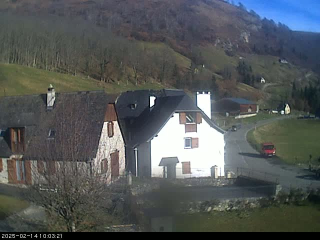A sunny day reveals a cluster of houses nestled in a valley, surrounded by barren, rolling hills.